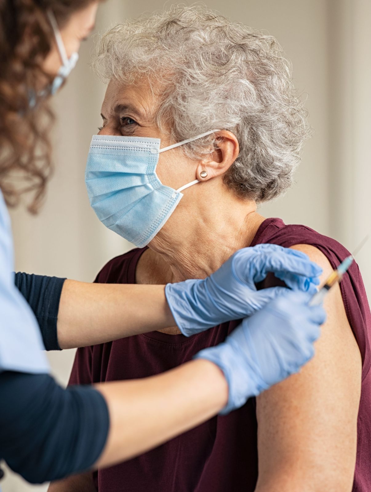 Ältere Dame mit blauer OP-Maske wird von Arzthelferin geimpft